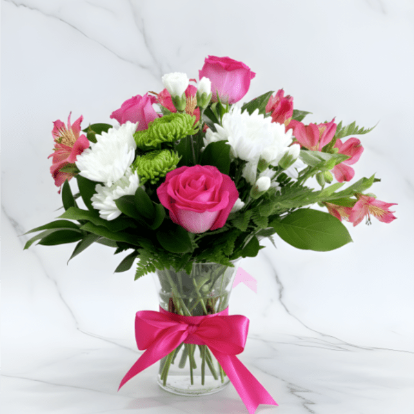 Pink roses and white blooms arranged in a glass vase with a pink ribbon
