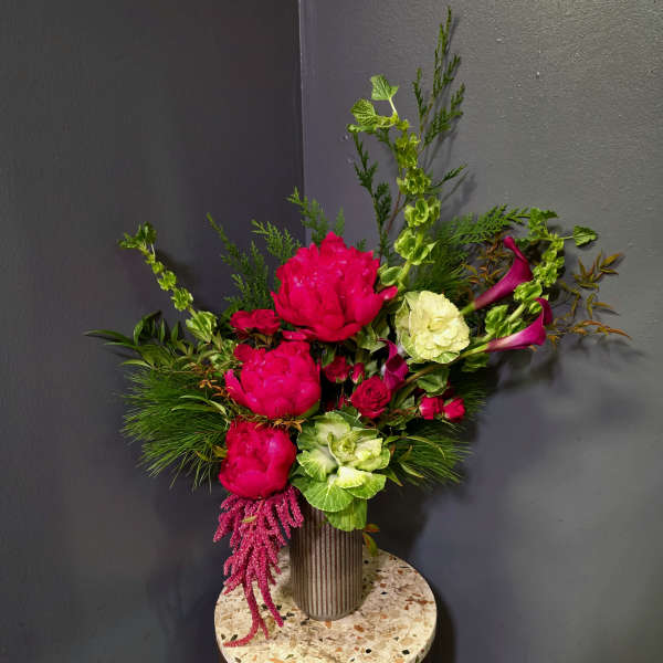 Bright pink floral arrangement in a ribbed vase with green accents
