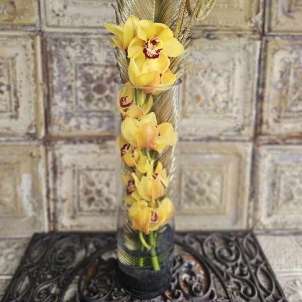 Yellow orchids in a tall glass vase with decorative feathers