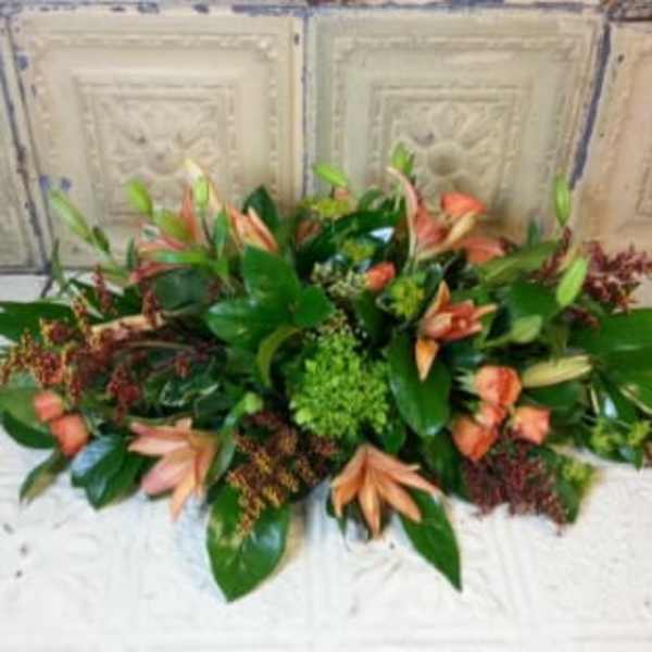 Low floral centerpiece with peach blooms and green foliage