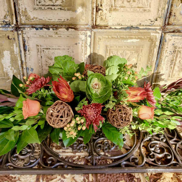 Low floral arrangement with peach roses and red blooms on a decorative metal stand