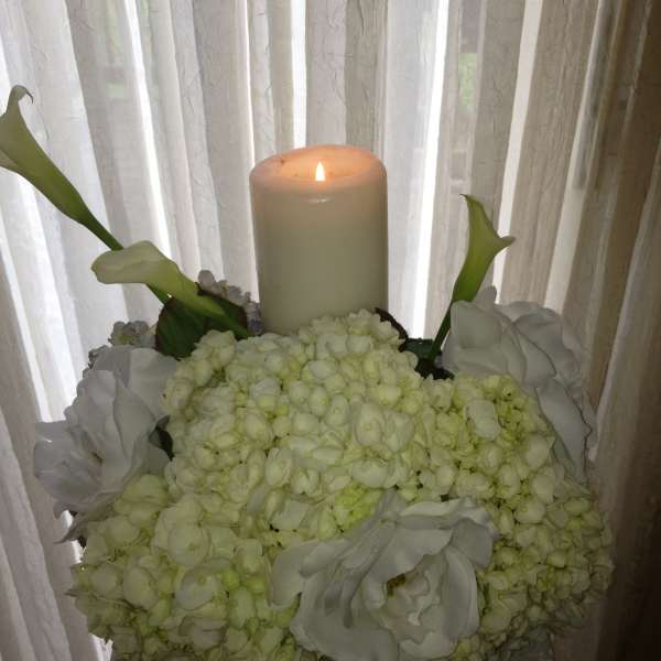 White floral arrangement with a lit pillar candle and calla lilies