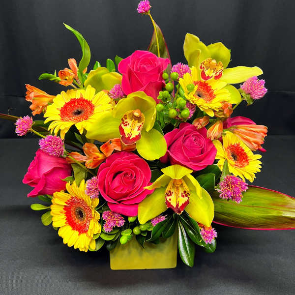Bright bouquet of pink roses, yellow orchids, and gerbera daisies in a square vase