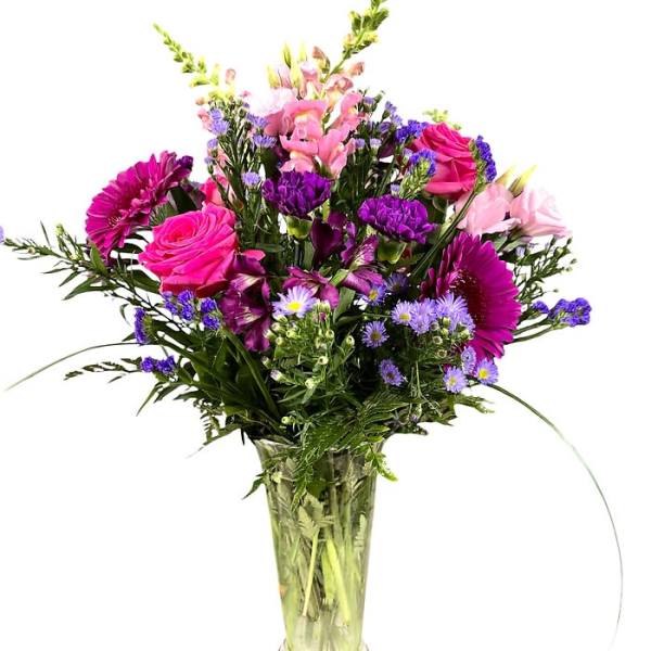 Tall mixed bouquet of pink roses and snapdragons with purple blooms in a clear glass vase