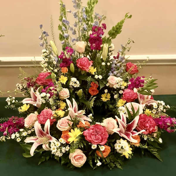 Large mixed floral arrangement with roses, lilies, and tall blue spikes