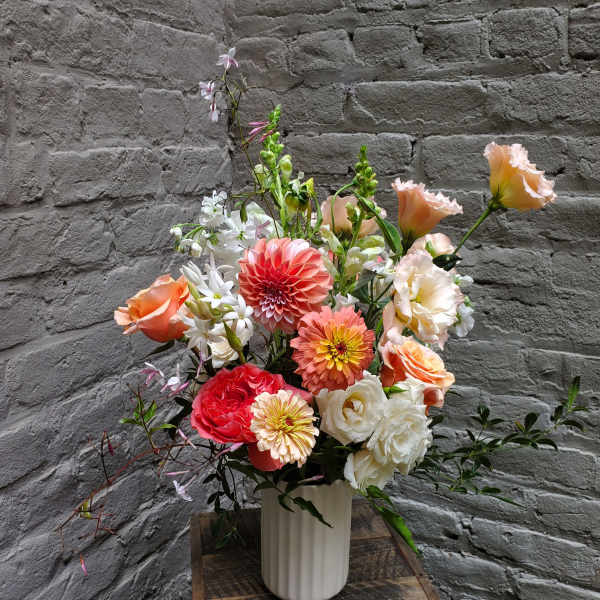 Mixed bouquet of coral, peach, and white flowers in a white vase