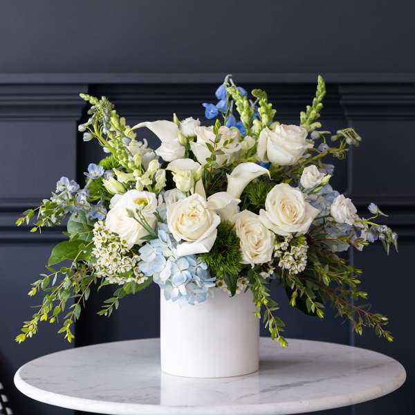 White roses and calla lilies in a white vase with blue accents