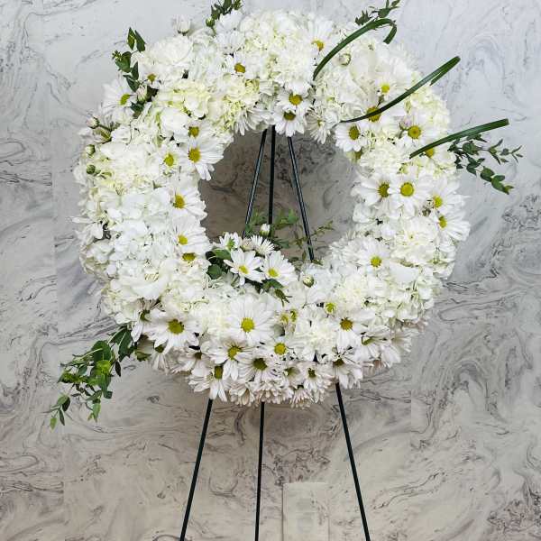White floral wreath on a black easel with daisies and hydrangeas
