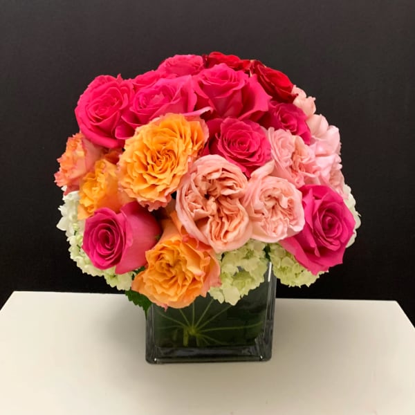 Bouquet of pink, peach, and orange roses in a square glass vase
