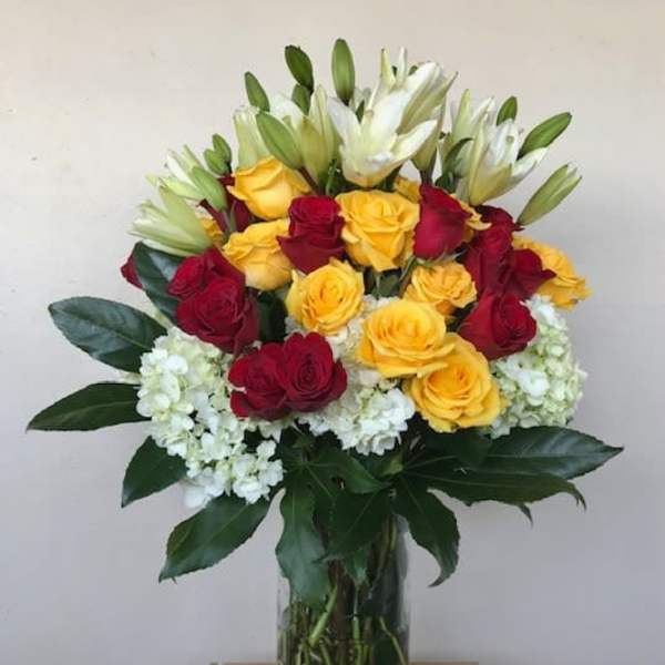 Bouquet of red and yellow roses with white lilies in a glass vase