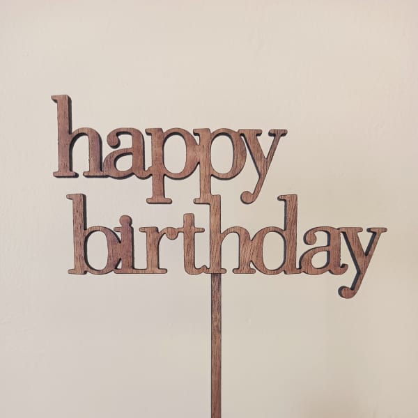 Wooden "happy birthday" cake topper held in a hand