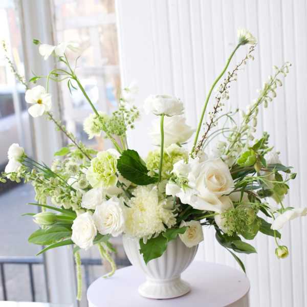 White floral arrangement in a white urn vase on a round pedestal