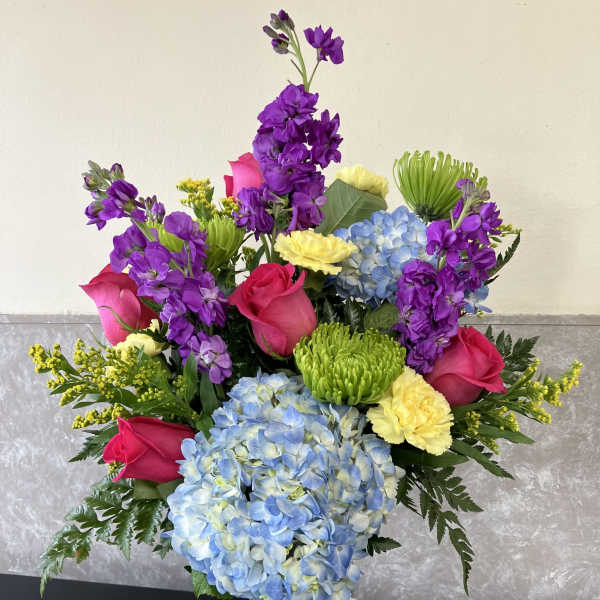 Colorful bouquet of roses, hydrangeas, and purple blooms in a glass vase