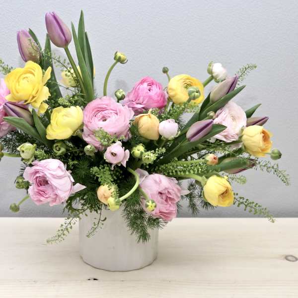 Pastel pink, yellow, and purple ranunculus and tulips in a white ceramic vase