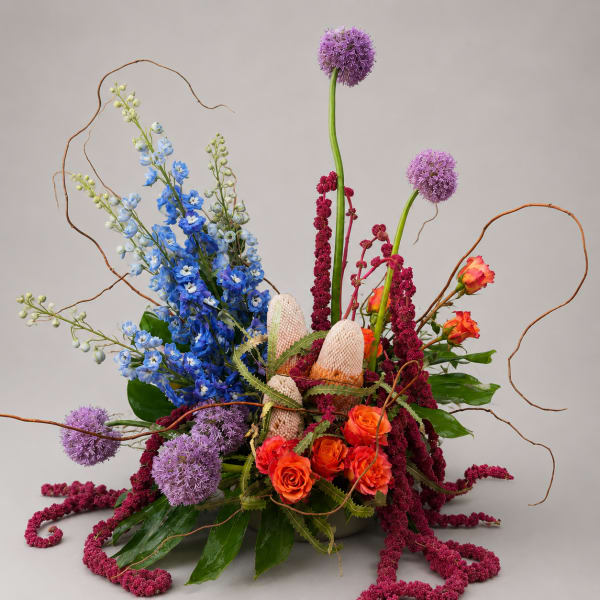 Tall floral arrangement with blue, purple, and orange blooms in a low container