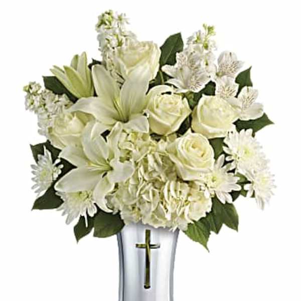 White lilies and roses arranged in a silver vase with a cross