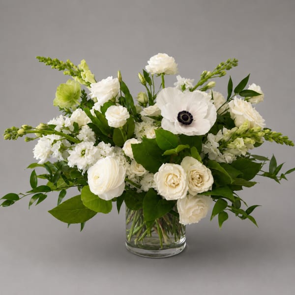White floral arrangement in a clear glass vase with green accents