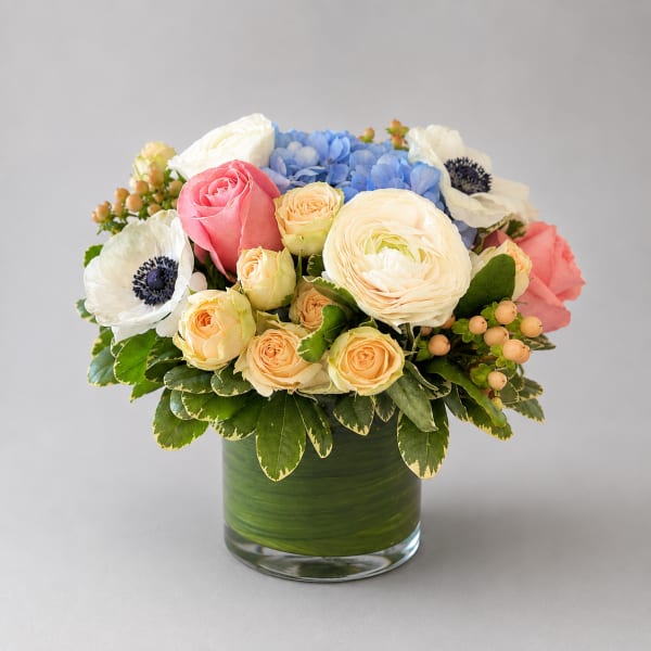 Mixed bouquet of roses, ranunculus, hydrangea, and anemones in a green glass vase