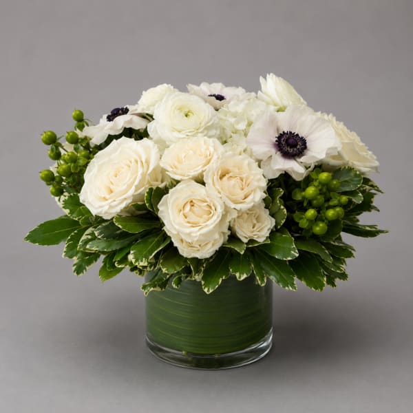 White roses and anemones arranged in a glass vase with green berries