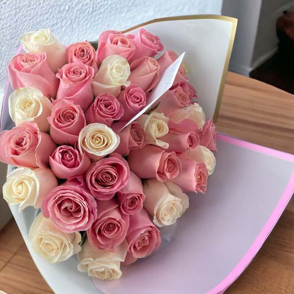 Bouquet of pink and cream roses wrapped in white paper with a card