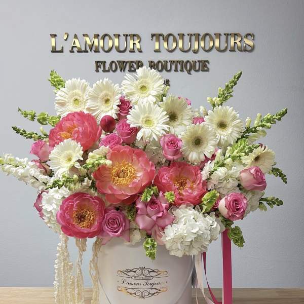 Pink and white flower arrangement in a white hat box with ribbons