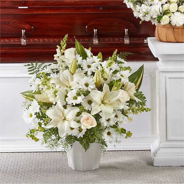 White funeral arrangement with lilies, daisies, and roses in a white vase