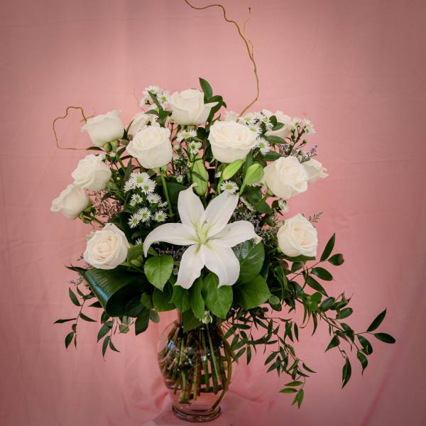 White roses and a white lily in a glass vase with small daisy flowers