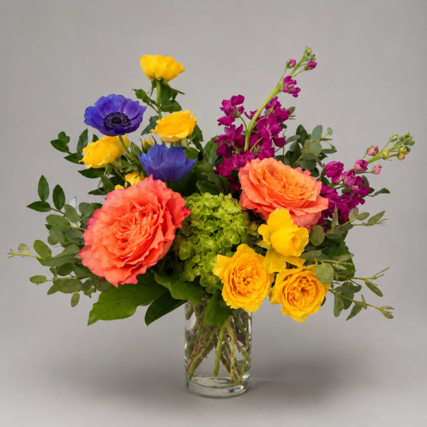 Colorful bouquet of roses, anemones, and orchids in a clear glass vase