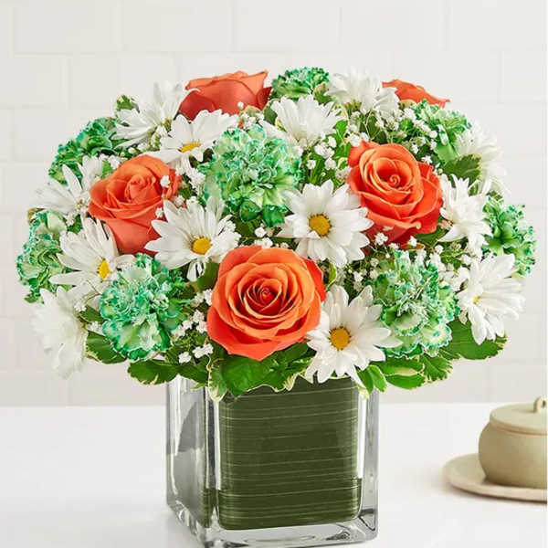 Orange roses and white daisies in a clear square vase