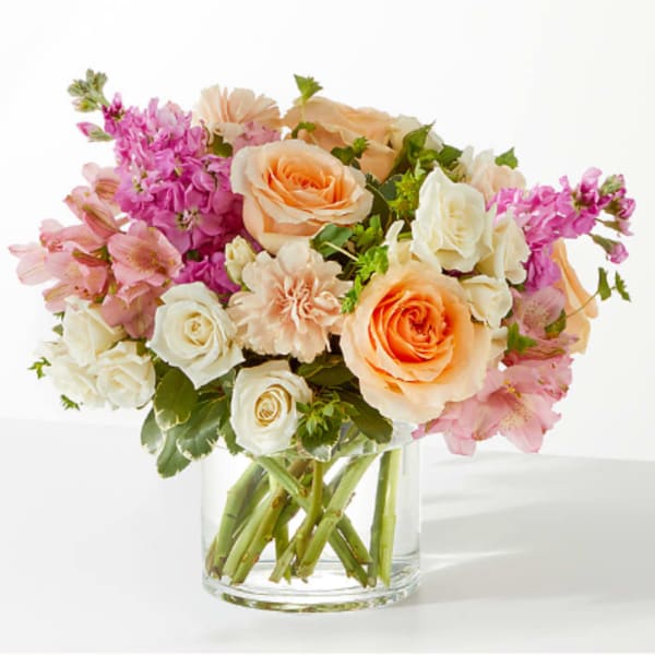 Bouquet of peach and white roses with pink flowers in a clear glass vase