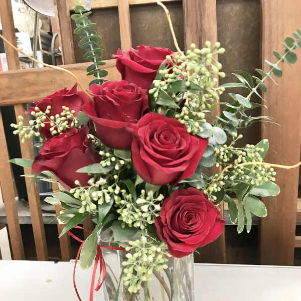 Red roses arranged in a clear square vase with greenery