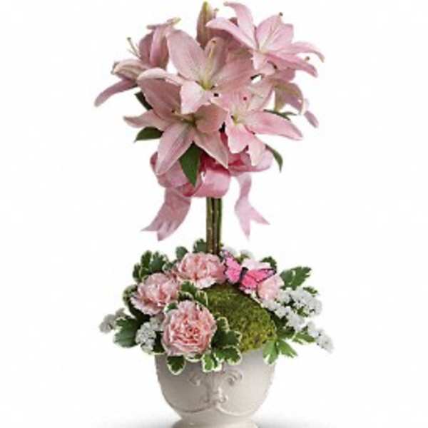 Tall pink lily topiary with pink carnations and white filler flowers in a white ceramic urn.