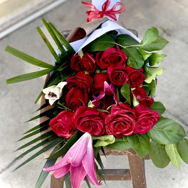 Bouquet of red roses with pink lilies and greenery wrapped in paper
