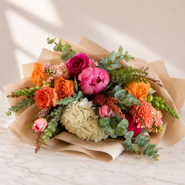 Mixed bouquet of roses, peonies, and hydrangea wrapped in kraft paper