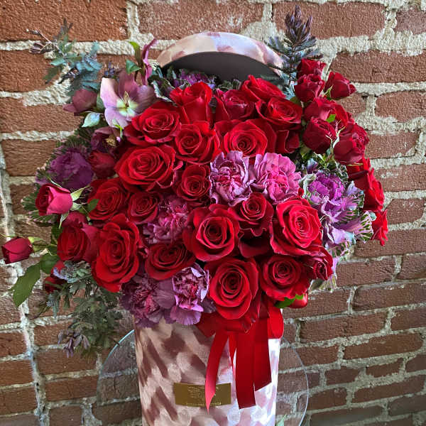 Red roses and pink flowers in a pink hatbox with a ribbon