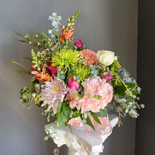 Mixed bouquet with pink, white, and green flowers in a pink container