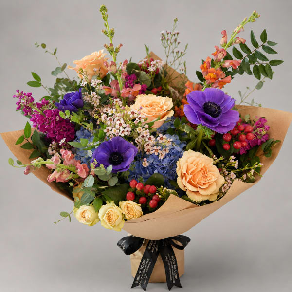 Mixed bouquet with purple anemones, peach roses, and blue hydrangeas in kraft paper