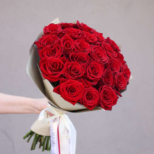 Bouquet of red roses wrapped in cream paper with a white ribbon