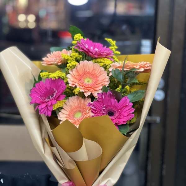 Bouquet of pink and peach gerbera daisies wrapped in cream paper with a pink ribbon
