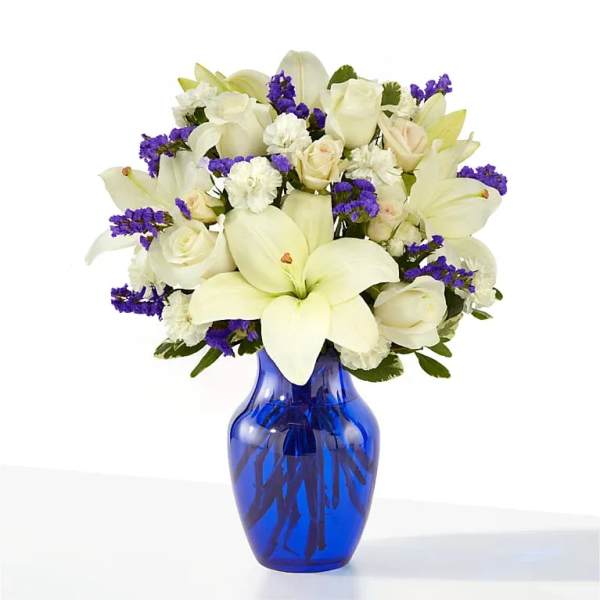 White lilies and roses in a blue glass vase with purple filler flowers
