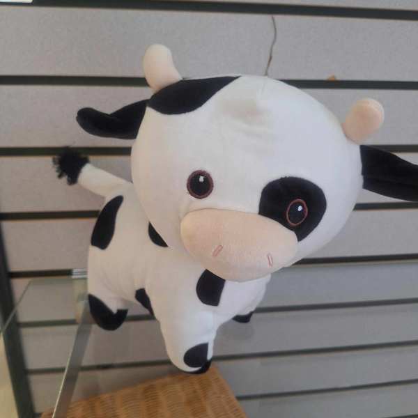 Small black and white cow plush toy with pink snout on a display shelf.