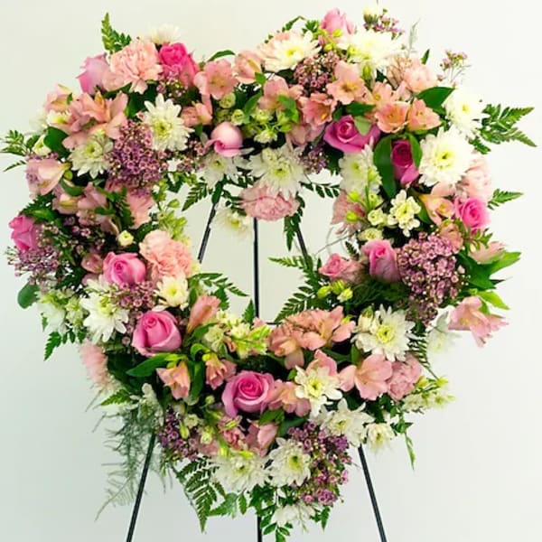 Heart-shaped floral wreath with pink and white flowers on a black stand