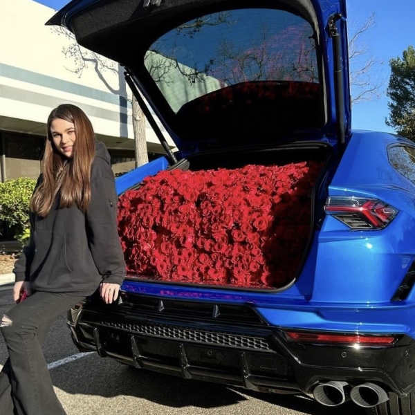Blue SUV with its trunk filled with red roses beside a woman