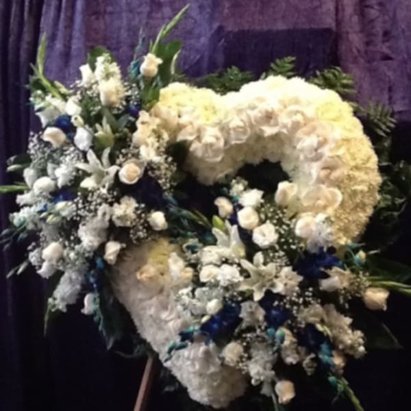 Large white floral funeral spray on an easel with blue accents