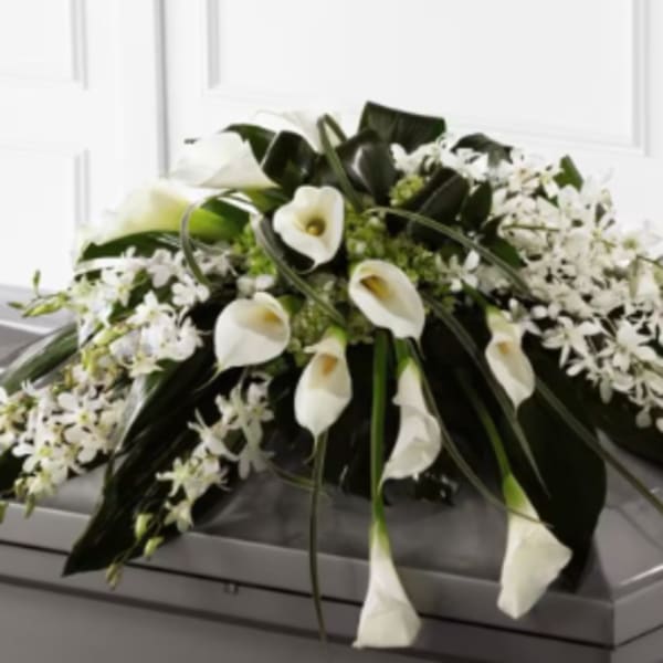 White calla lilies and orchids arranged on a gray casket