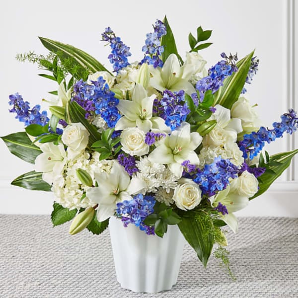 White lilies and roses with blue flowers in a white vase