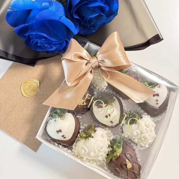 Blue roses with a box of chocolate-covered strawberries and a ribbon