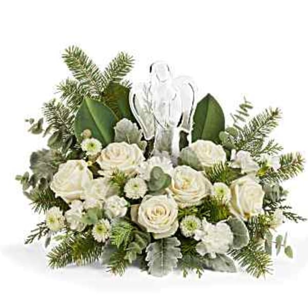 White roses and greenery arranged around a clear angel figurine