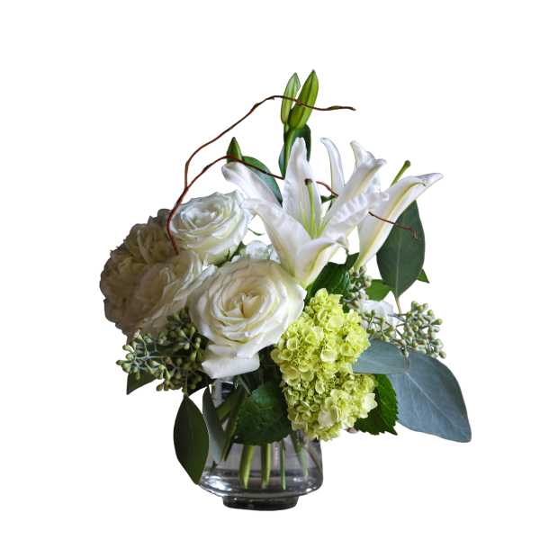 White lilies, roses, and green hydrangeas arranged in a clear glass vase
