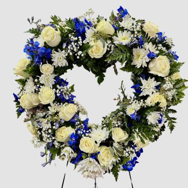 Heart-shaped floral wreath with white roses and blue flowers on a stand